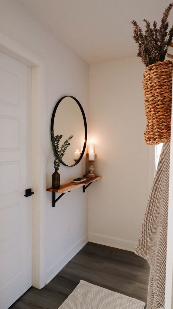 A cozy and stylish hallway with a round mirror, shelf, and natural decor elements.