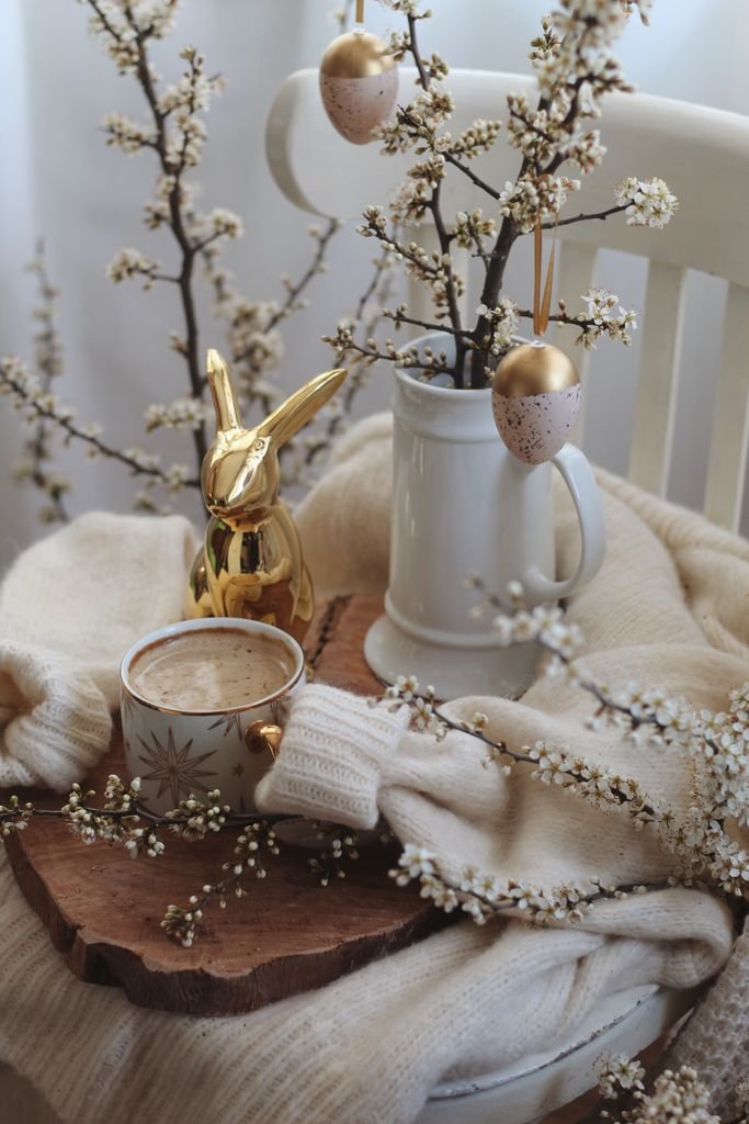 Cup of hot coffee placed on wooden tray with Easter decorations on white chair in light room during holiday celebration