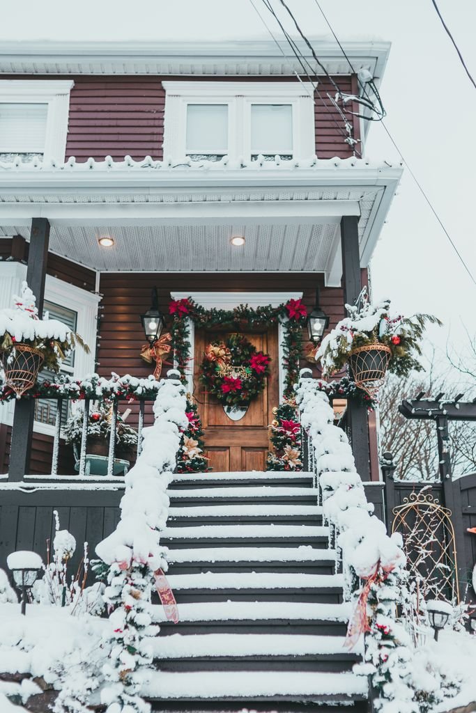 New Year decor with wreath and garland on door of dwelling house with snow on stairs in wintertime