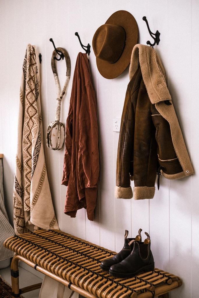 Warm rustic entryway with hanging coats, hat, and boots on a bench, perfect for autumn decor.