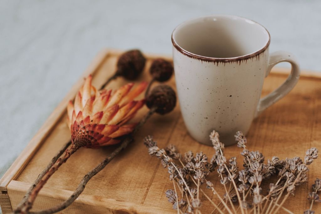 A cozy scene featuring a rustic mug paired with dried flowers on a wooden tray.