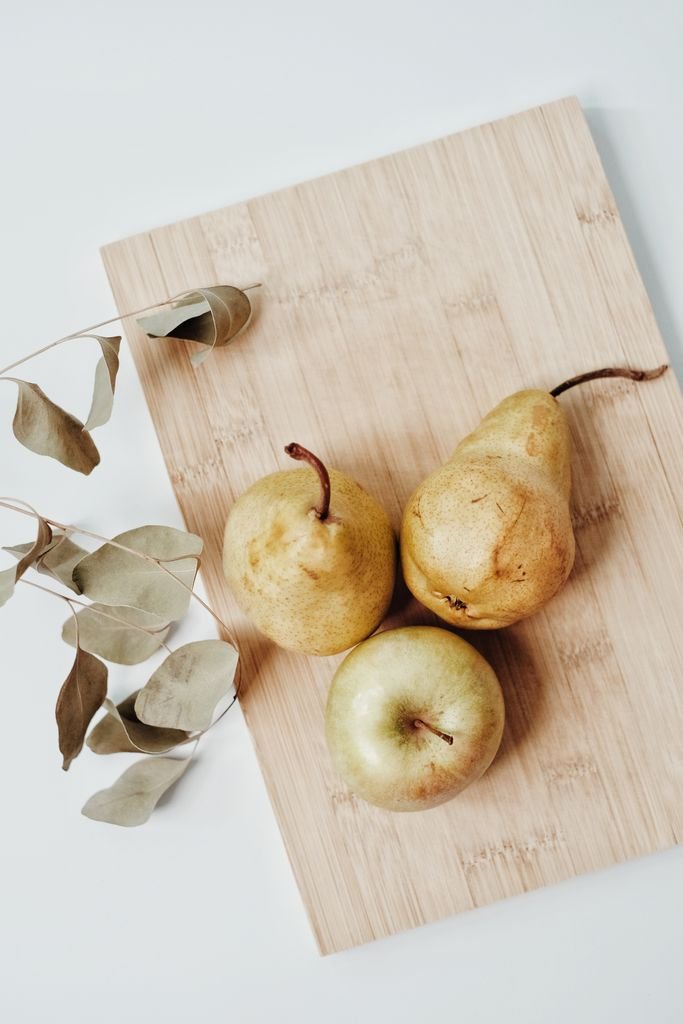 Three ripe pears placed on a wooden board with dried leaves. High angle shot.