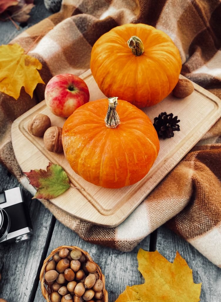 Top view of pumpkins, apple, and nuts on a rustic board, evoking autumn charm.
